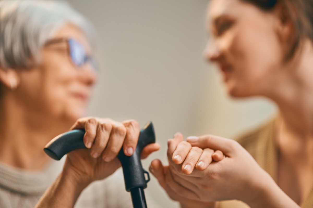 Personne âgée tenant une canne échangeant avec une professionnelle qui lui tient la main