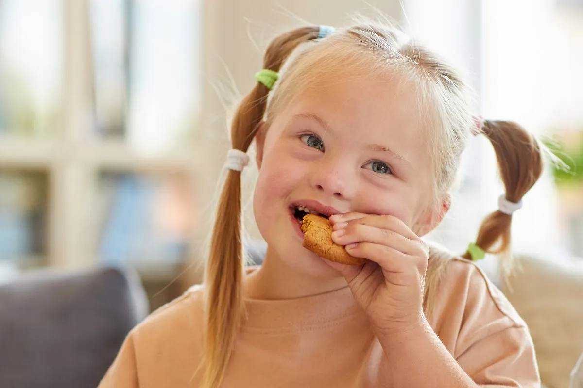 Jeune fille en situation de handicap mangeant un biscuit à la maison, illustrant un article sur le projet personnalisé de scolarisation