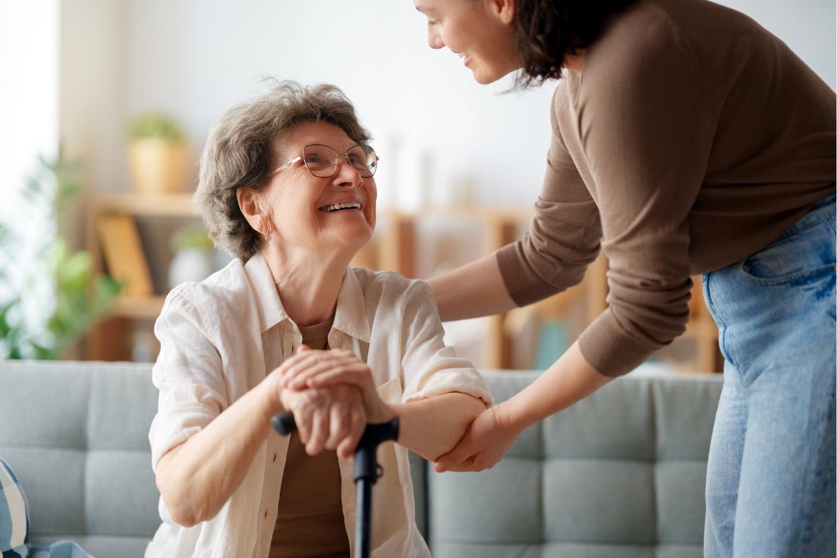 Personne âgée souriante aidée par une accompagnante à domicile