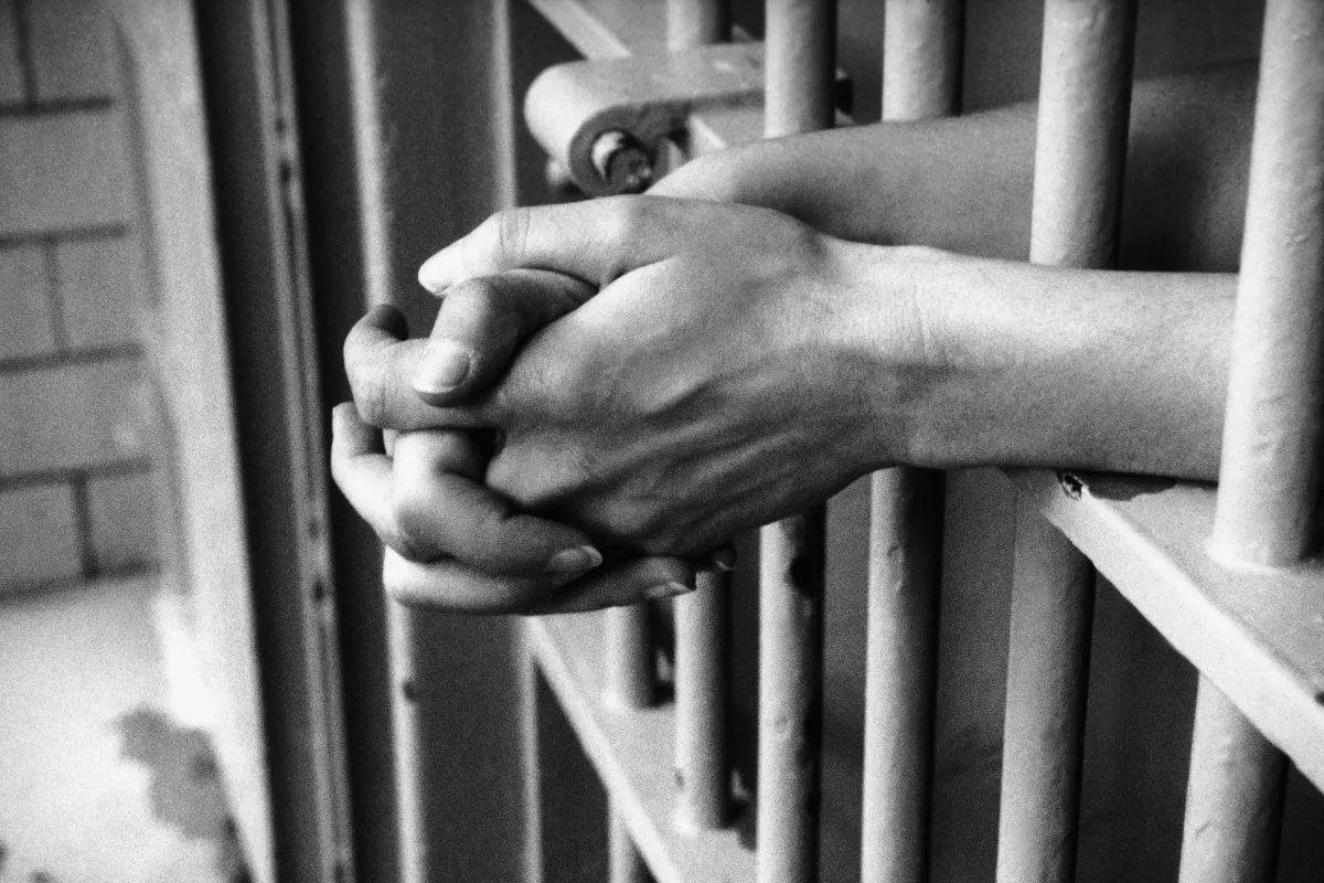Mains croisées derrière des barreaux illustrant le milieu carcéral