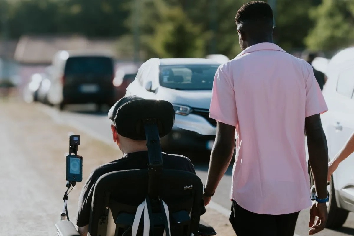 Accompagnant marchant aux côtés d’une personne en fauteuil roulant, illustrant l’accompagnement de la maladie de Charcot à domicile