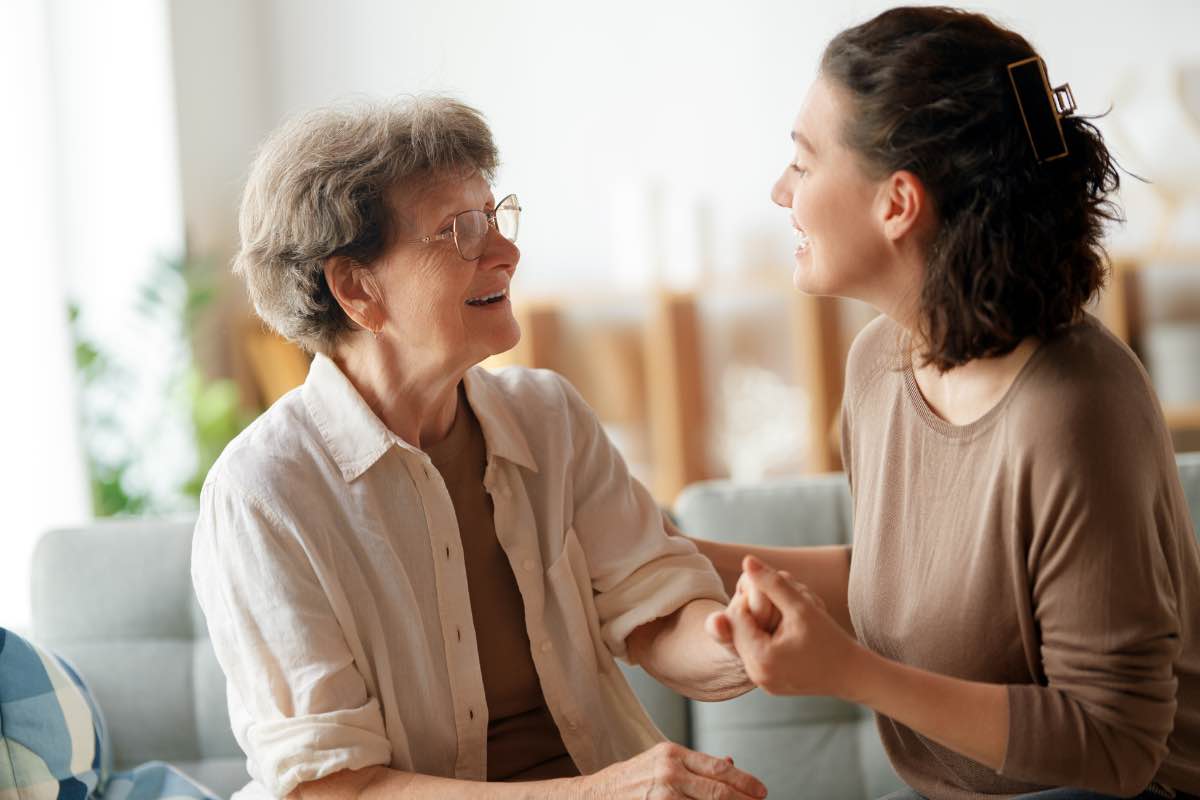 une personne âgée à son domicile avec une auxiliaire de vie se tenant la main