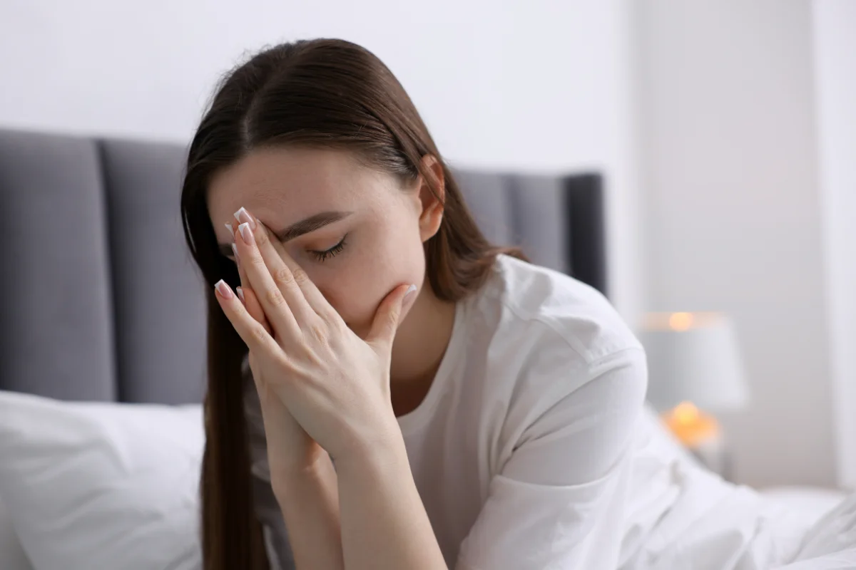 Femme épuisée assise sur son lit, illustrant la charge mentale et le besoin de déléguer les tâches à domicile